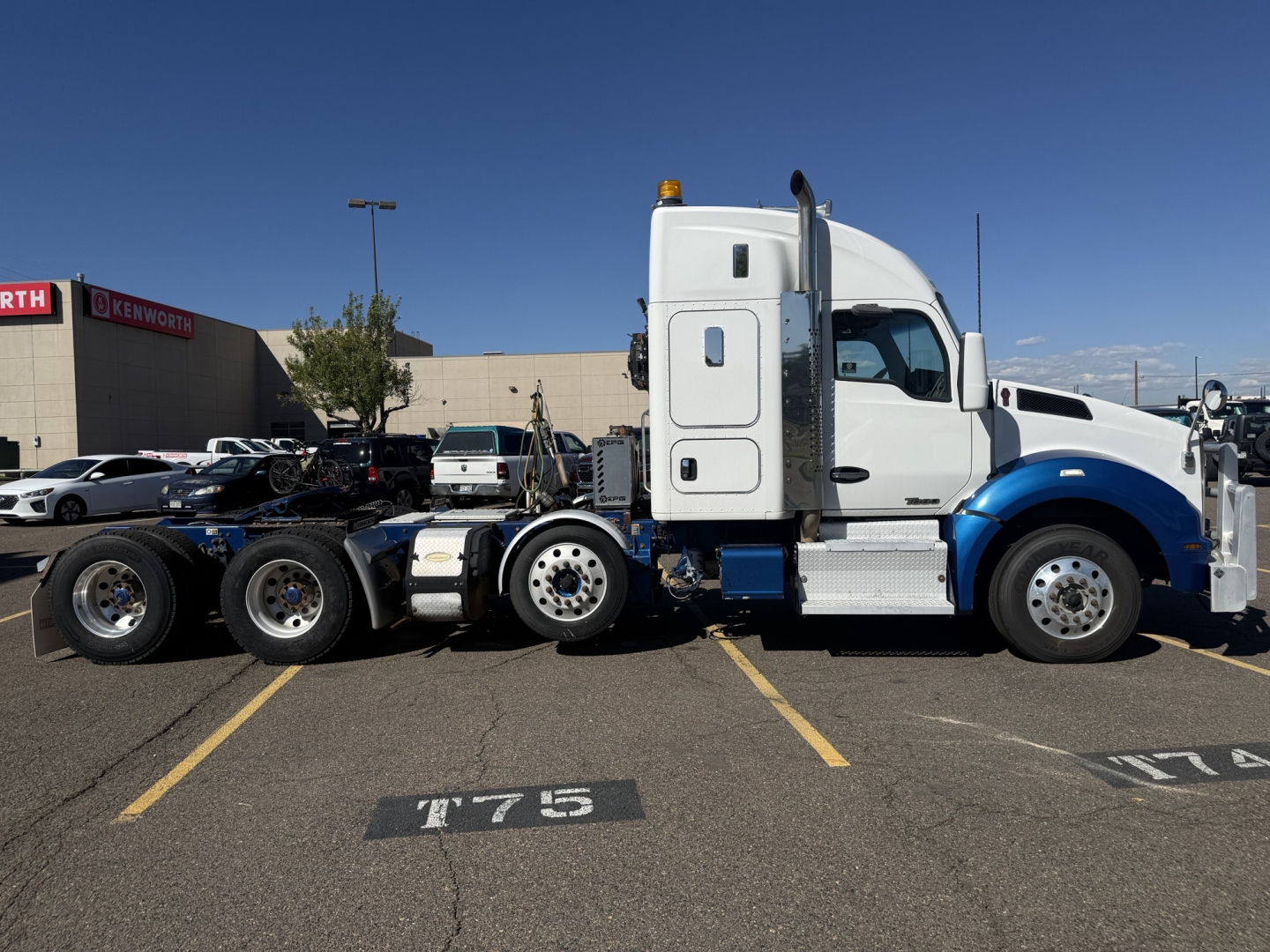 Kenworth T880 tractor in side profile showing aluminum fuel tanks and cab with sleeper, blue front fenders, chrome steps, and fifth wheel.