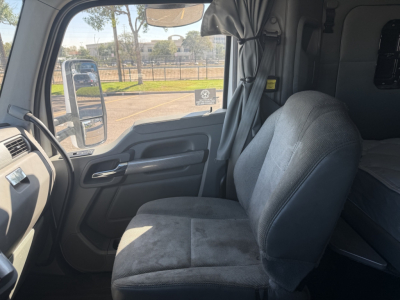 Kenworth T880 cab interior left-side dash and driver seat in view, with window and mirror reflections.