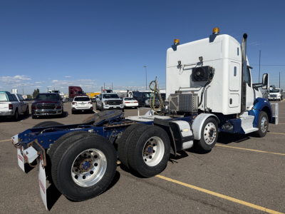 Kenworth T880 cab over engine truck rear chassis view showing triple rear axles and white sleeper cab.