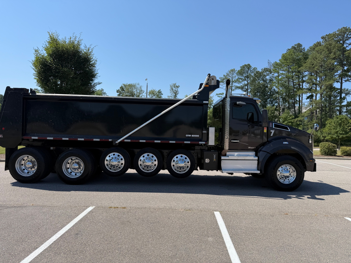 Kenworth T880 dump truck side view showing black dump bed, dual rear axles, chrome wheels, and cab with step access.