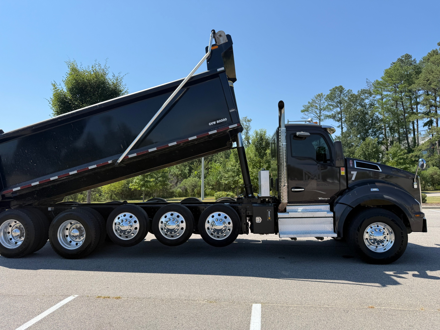 Kenworth T880 dump truck side view showing black cab, long multi-axle chassis, and raised dump bed. No visible text readable on components.