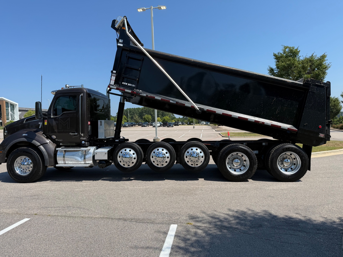 Kenworth T880 dump truck side view showing black dump bed raised with multi-axle rear wheels and chrome fuel tanks.
