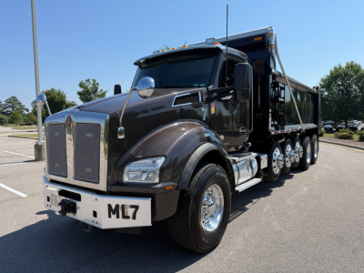 Kenworth T880 dump truck in a parking lot, black color, front grille with Kenworth emblem, large headlights, ML7 license plate on front bumper, dual rear axles, dump bed visible.