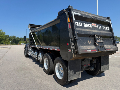 Kenworth T880 dump truck rear and side showing 111 feet Stay Back ARMR signaling banner on tailgate and multiple rear axles.