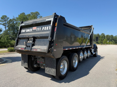Kenworth T880 dump truck rear-and-side view showing dump bed, dual rear axles, and stay back decals.