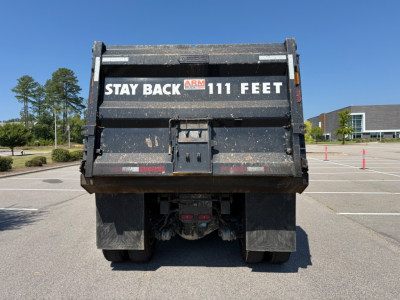 Kenworth T880 dump truck rear showing 'STAY BACK 111 FEET' warning on tailgate and mud flaps in a parking lot.