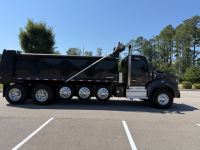 Kenworth T880 dump truck side view showing black dump bed, dual rear axles, chrome wheels, and cab with step access.