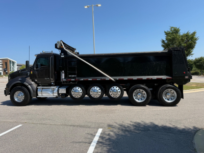 Kenworth T880 dump truck side view showing black dump body, multi-axle rear with six wheels, hydraulic lifting mechanism, chrome fuel tanks, and sleeper-less cab.