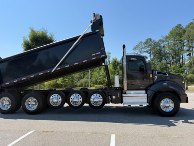 Kenworth T880 dump truck side view showing black cab, long multi-axle chassis, and raised dump bed. No visible text readable on components.