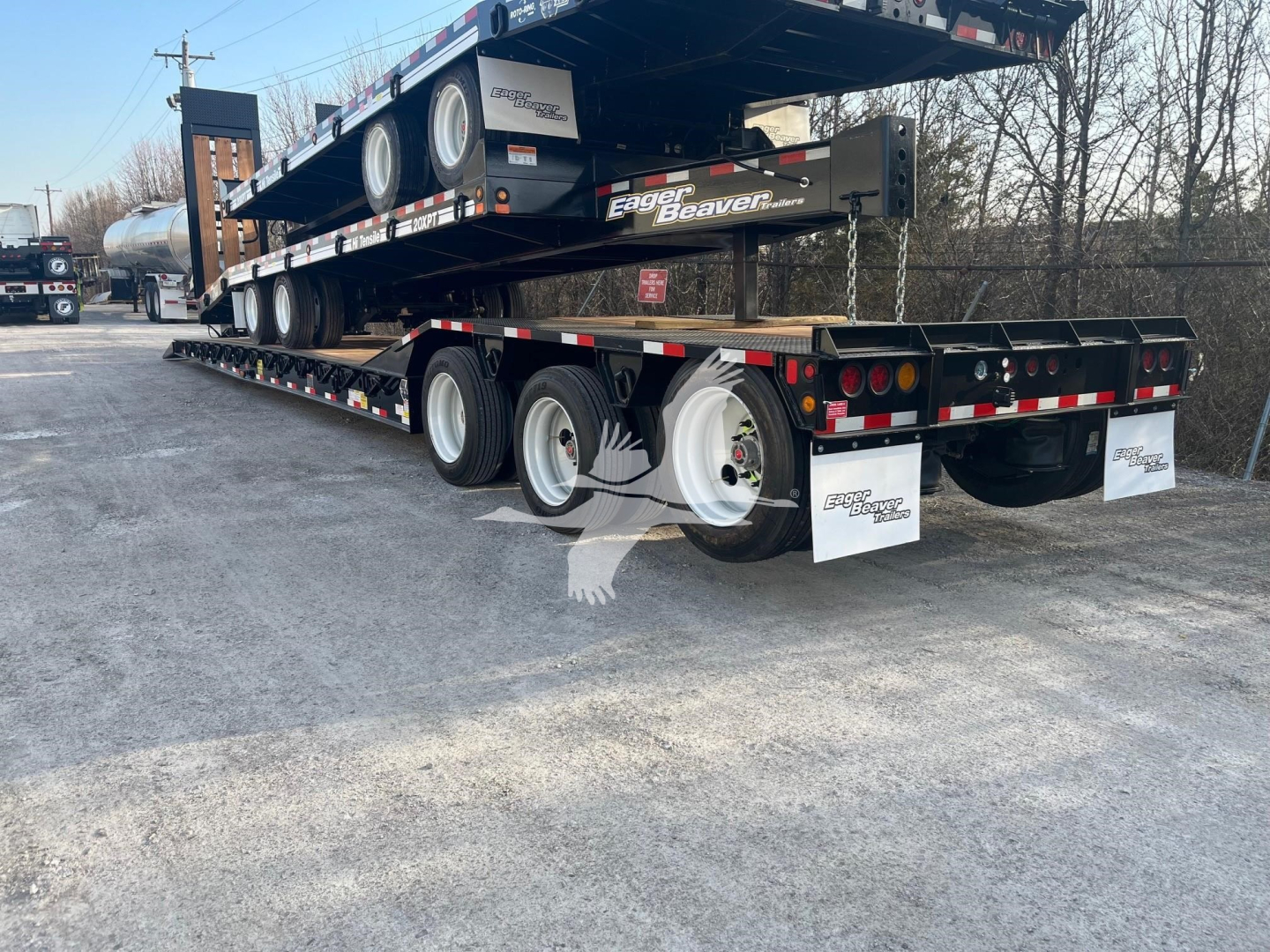 Trailer showing flatbed lowboy with multiple axles and wheels, Eager Beaver logo on side, rear mud flaps, and reflective safety markings.