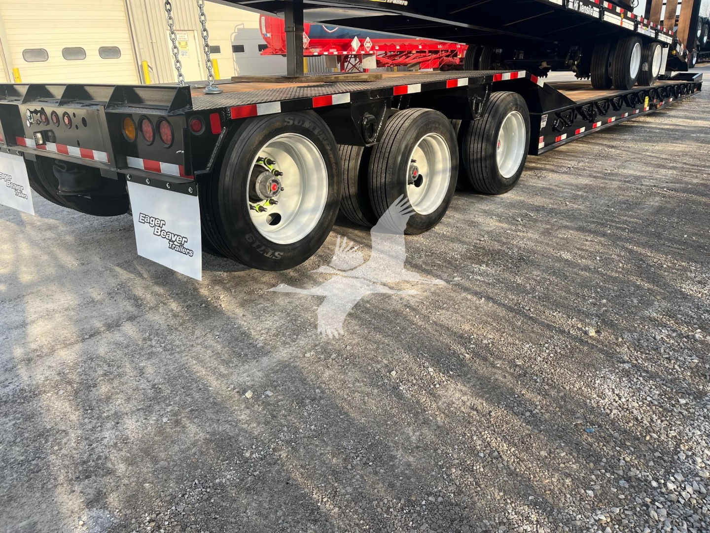 Trailer undercarriage showing multiple axles and tires with mud flaps; chrome wheels; side rails; reflective tape; some white mud flaps with graphics