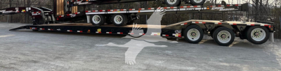 Trailer with lowboy deck showing multi-axle configuration and loading ramp, side rails, and branding visible.