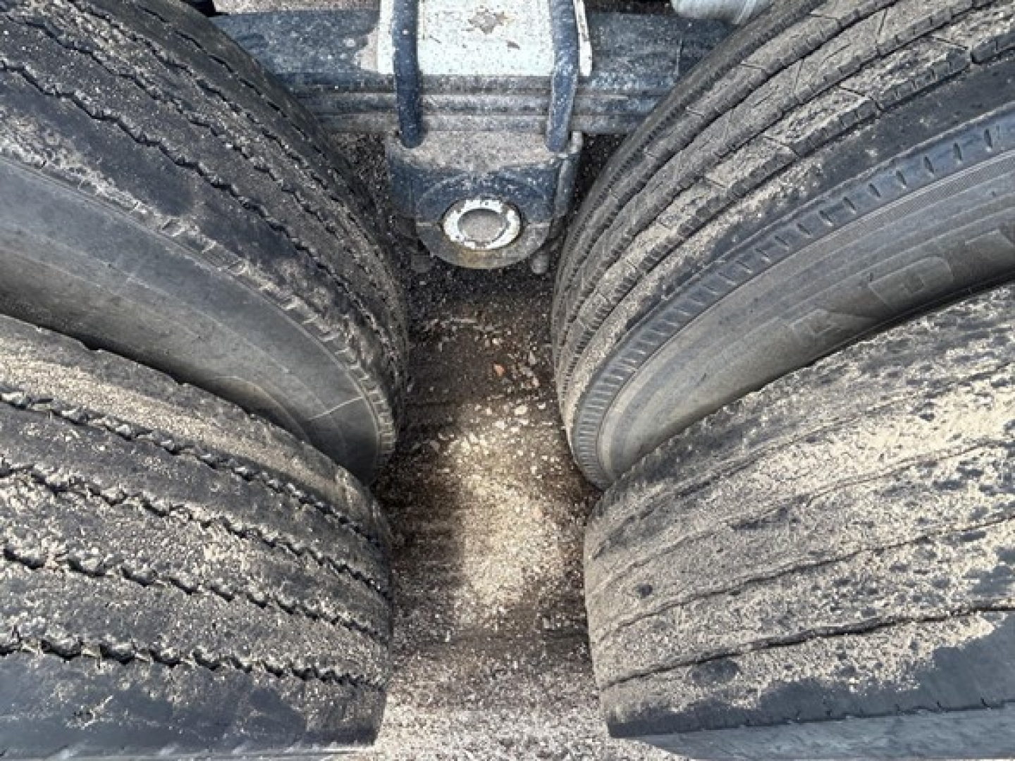 Dump trailer axles with dual wheels showing dirt and wear between tires.