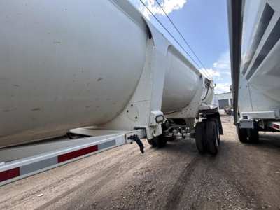 Dump trailer showing side view with cylindrical tank and wheels, text not visible.
