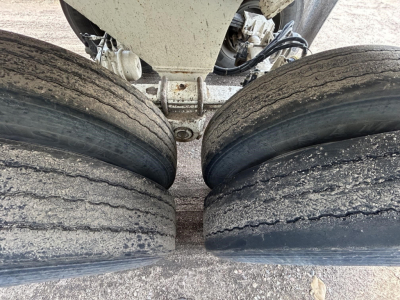 Dump trailer axle close-up with two worn rear tires and suspension components visible between the wheels.