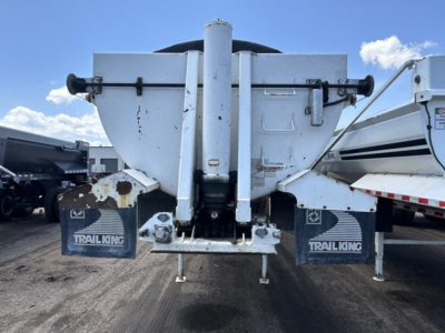 Rear view of a dump trailer showing a vertical hoist mechanism, two TrailKing mud flaps, and hydraulic components; some rust and wear marks visible.
