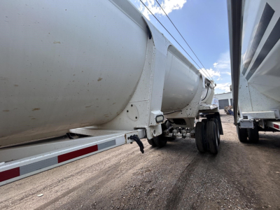 Trailer side view showing cylindrical tank on a dump trailer with wheels and frame visible.