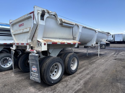 Dump trailer side view showing Ranco ED26-34 logo on rear, dual rear axles with tires, white/gray steel body, reflective tape, and mud flaps.