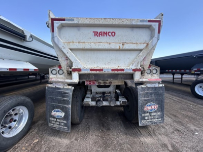 Dump trailer rear showing RANCO logo on tailgate and dual axles with mud flaps and undercarriage components.