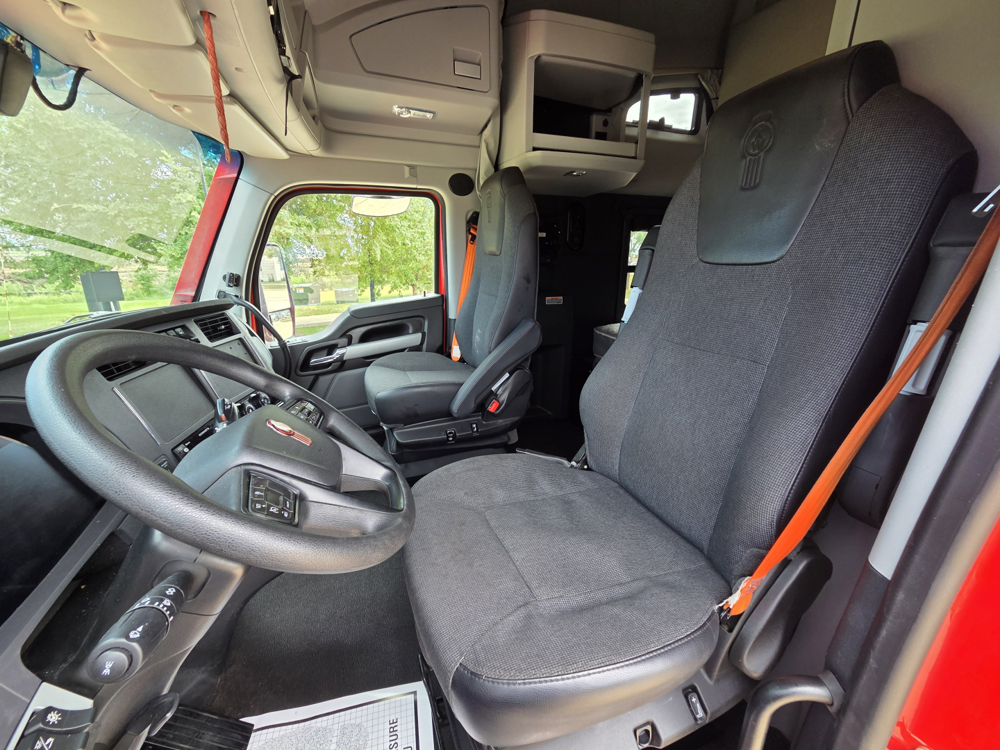 Kenworth T680 truck cabin interior showing driver seat and dashboard with steering wheel and overhead storage.