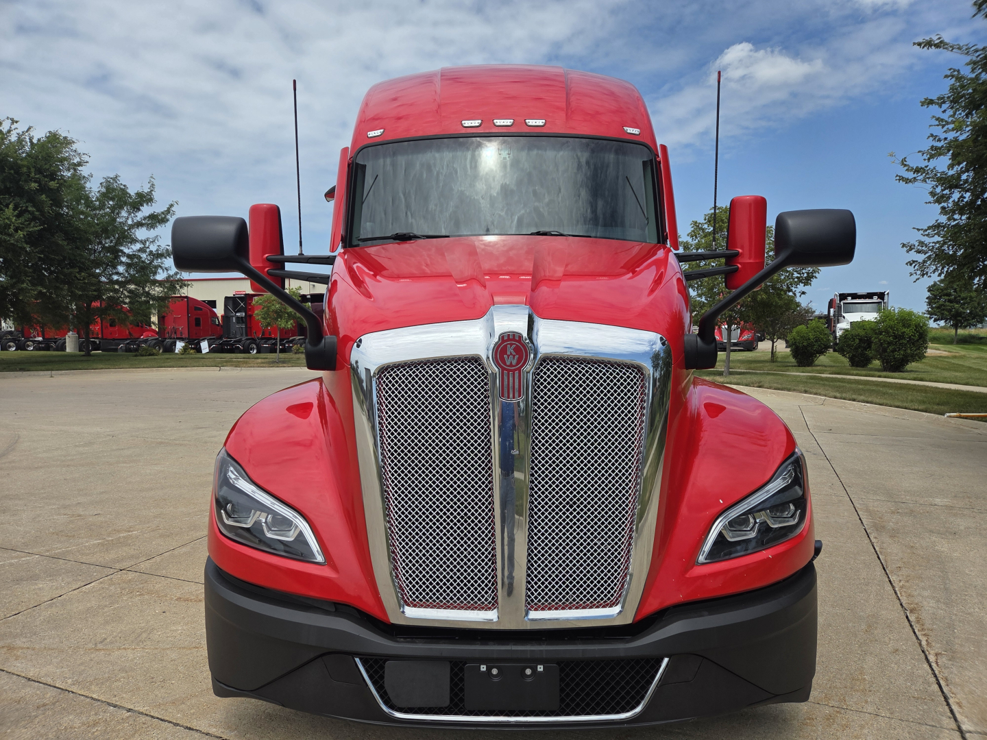Kenworth T680 front view showing red truck with large chrome grille and black bumper, headlights, and mirrors.