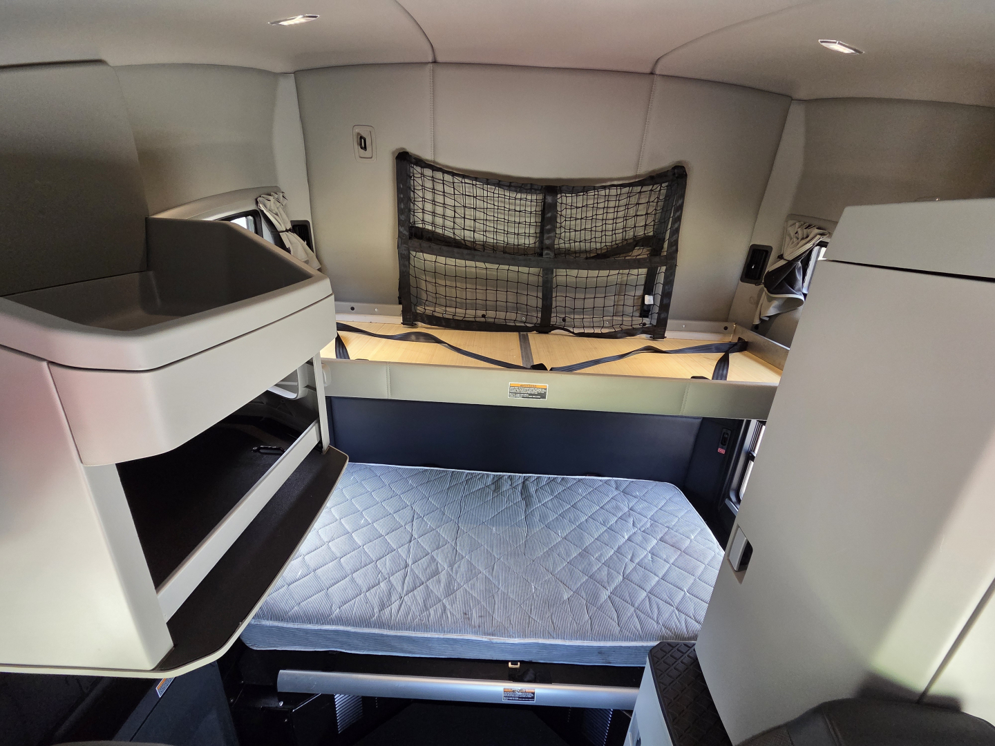 Kenworth T680 sleeper cab interior showing bunk beds and storage compartments with a quilted mattress and netting across the wall.