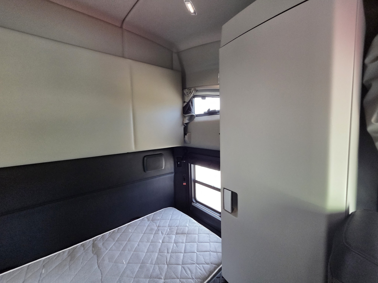 Interior sleeper cab of a Kenworth truck with a bunk bed and storage cabinet visible.