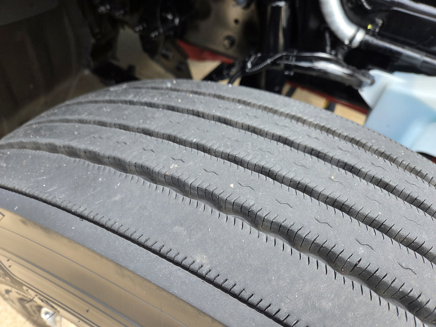 Kenworth T680 drivetrain area showing a close-up of a tire tread on a heavy truck, with parts of the engine bay and undercarriage in the background.
