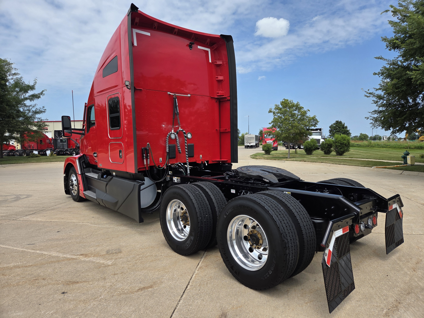 Kenworth T680 tractor rear/side view showing red sleeper cab, dual rear axles, mudflaps, and metal steps.