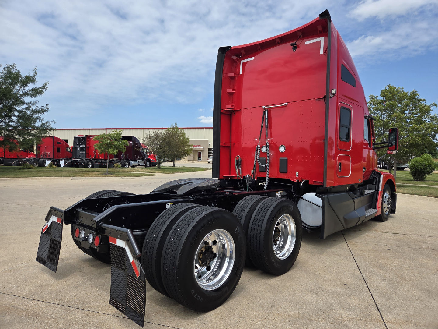 Kenworth T680 side/rear view showing red sleeper cab, dual rear axles, black chassis, and fifth wheel with mud flaps.
