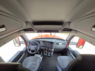 Kenworth T680 cab interior view from driver seat showing steering wheel, dashboard, and front seats. Cabin details visible with sun visors and overhead storage.