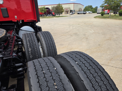 Kenworth T680 chassis and dual rear wheels seen from side, with red cab and gravel lot in background.