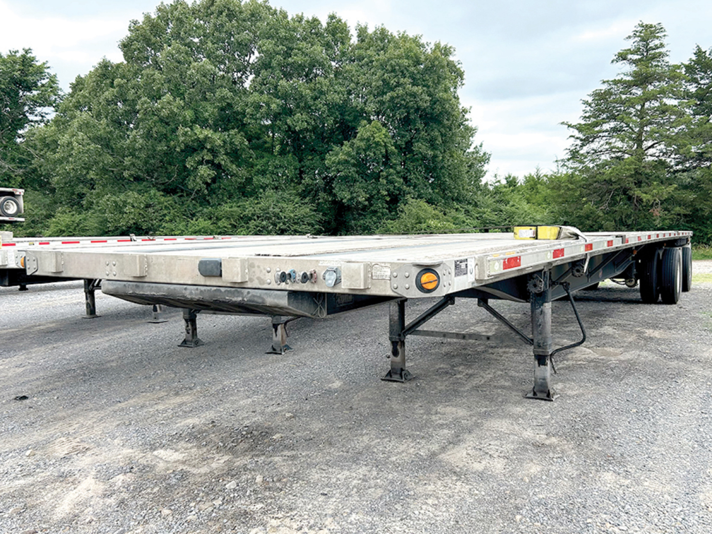 Flatbed trailer showing aluminum and steel composite construction with support legs and dual axles in an open lot.