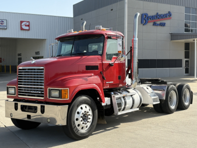 Truck image: red 2015 Mack CHU613 Daycab tractor showing front grille, dual headlights, chrome bumper, and side fuel tank, on lot in front of dealership building.