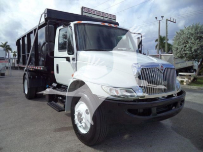 Truck front left view showing International Durastar 4300 dump/roll-off body with chrome grille, white cab, black dump body, round headlights.