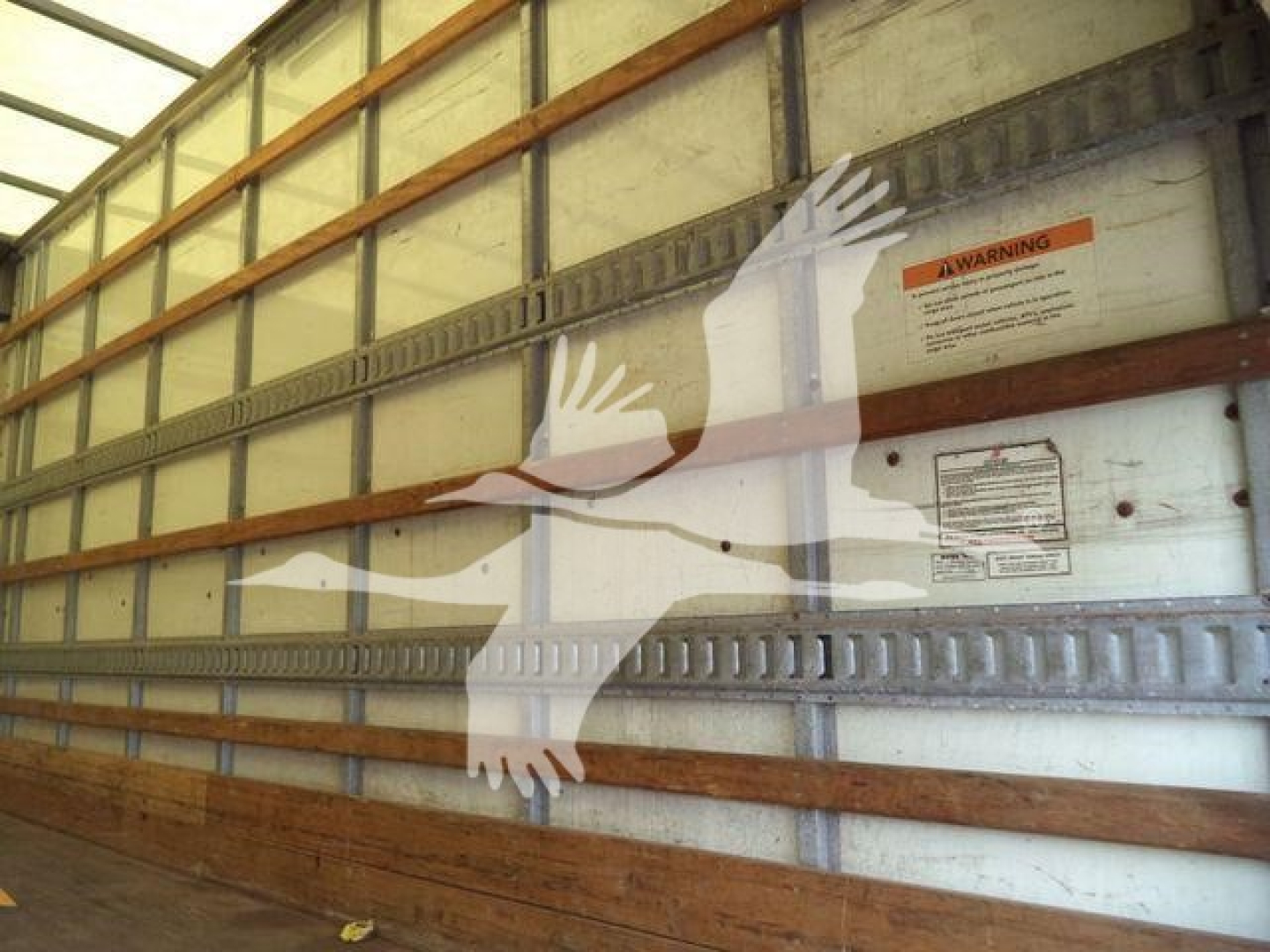 Isuzu NPR HD truck box interior wall with warning label and stamped metal wall; no engine text visible.
