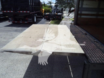 Platform truck bed with loading ramp extended, Isuzu NPR HD context; visible dirt and a hand silhouette watermark overlay in the foreground.