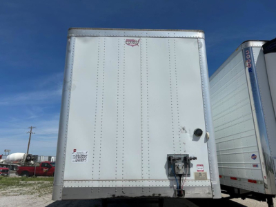 Rear view of a white 2016 Wabash trailer showing back doors, locking mechanism, and small decals. Clear sky with other trailers in the background.