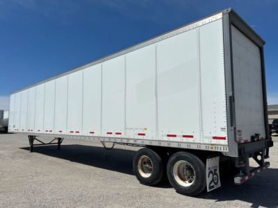 Trailer side view showing a white 2016 Wabash van trailer with tandem axles and reflective tape along the lower edge.