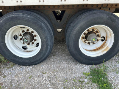 Dual rear wheels of a trailer showing white rims with rust and green valve stems.