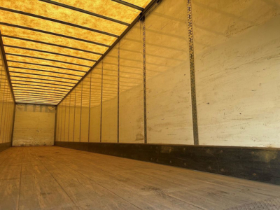 Trailer interior showing empty cargo space with wooden floor and metal side walls, yellow light from translucent roof panels.