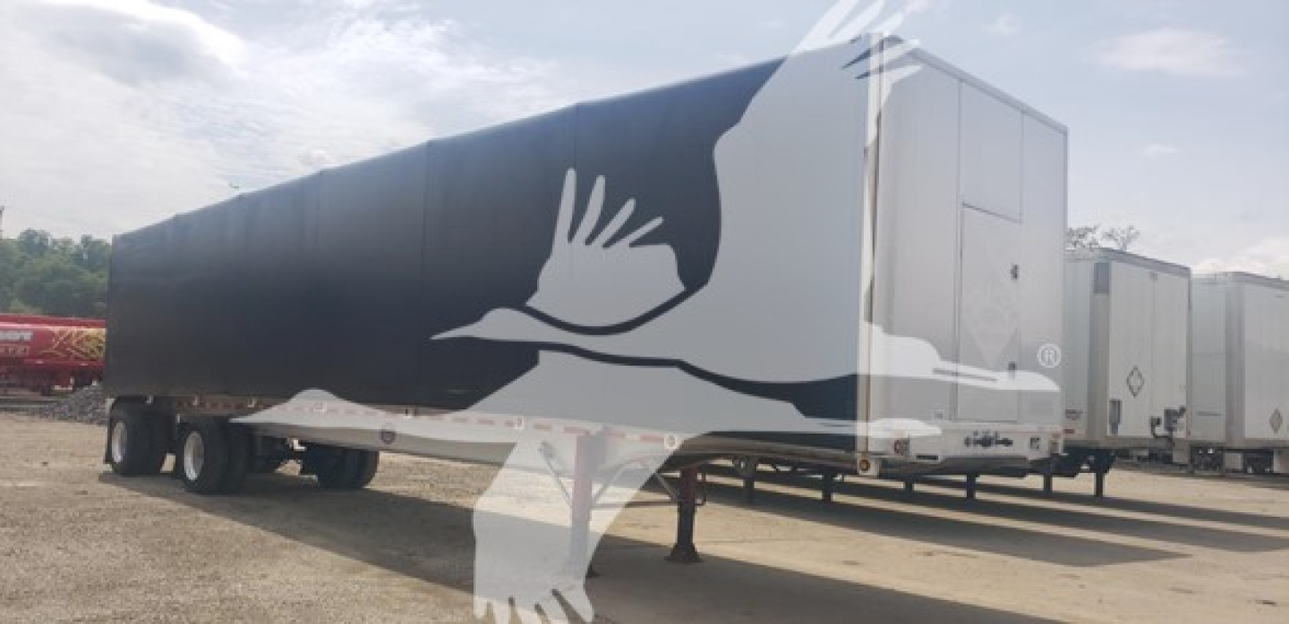 Trailer side with large white crane-like bird graphic and black curtain side; front cab and landing gear visible; no legible text.