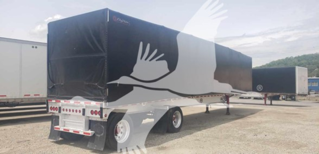 Trailer showing a mac aluminum flatbed curtainside with a white bird graphic on a black cover.