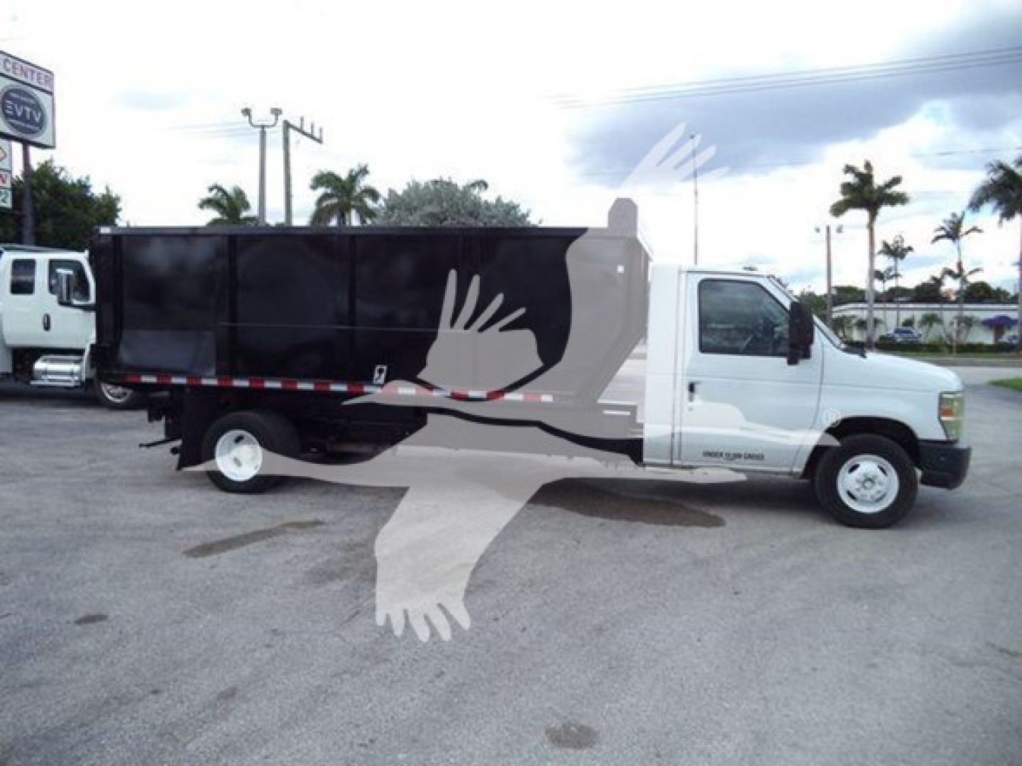 Ford E-450 dump truck side view showing black dump bed and white cab with stock number T10516 visible.