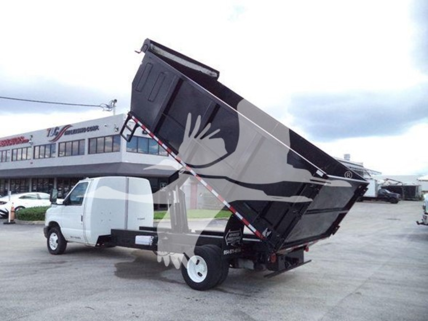Ford E-450 dump truck with raised dump bed and white cab, side view showing hydraulic lift.