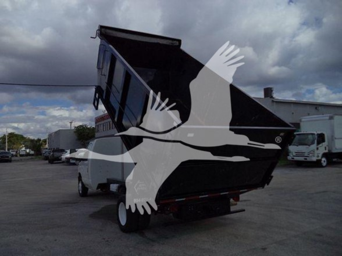 Dump truck bed of a Ford E-450 with a raised dump body in a yard, with a watermark of a bird across the image.