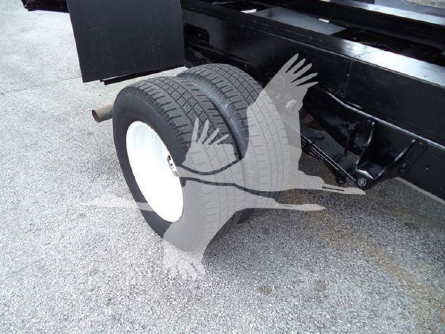 View of rear wheels and suspension on a Ford E450 dump truck chassis. Dual rear tires with white rims. Some undercarriage components visible.