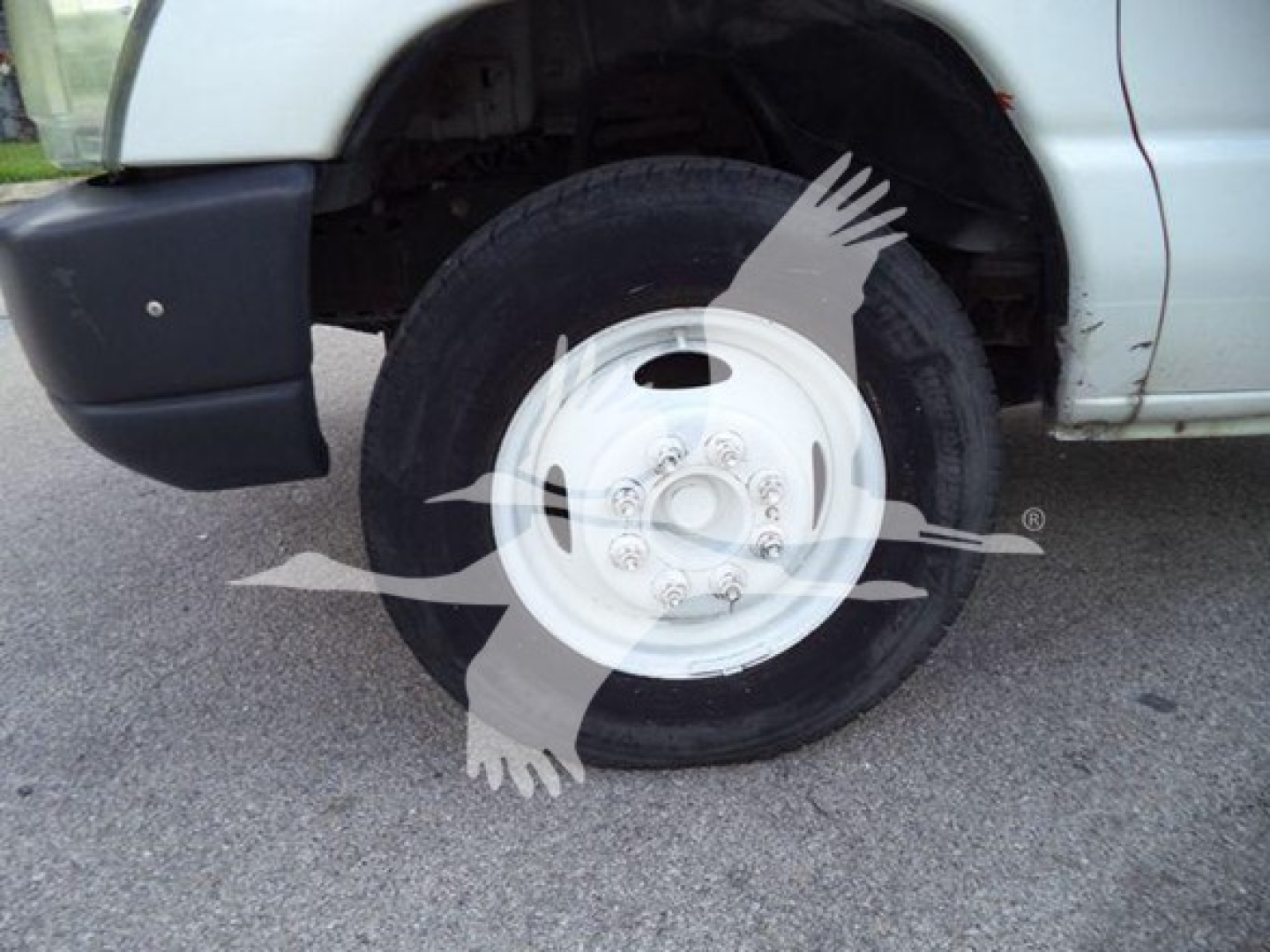 Ford E-Series truck front wheel and fender with white steel wheel and tire, exposed undercarriage slight rust around wheel well area.