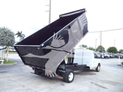 Ford E-Series dump truck with raised dump bed showing side and rear. Visible text on rear bumper/side panels includes stock/ID numbers, no specific model details legible.