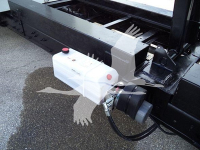 Ford E-450 dump truck hitch area with white plastic reservoir and hydraulic hose, visible black chassis and mounting hardware.